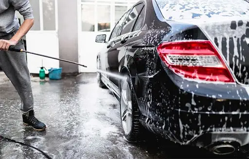 Homem lavando carro com pressão e espuma.
