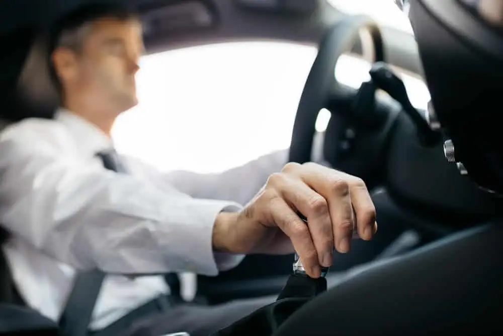 Homem dirigindo carro com foco na mão no câmbio.