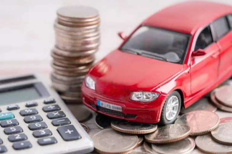 Carro em miniatura sobre moedas e calculadora