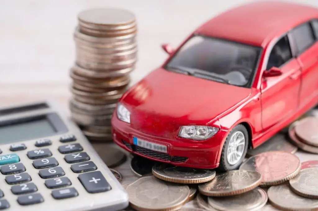 Carro em miniatura sobre moedas e calculadora