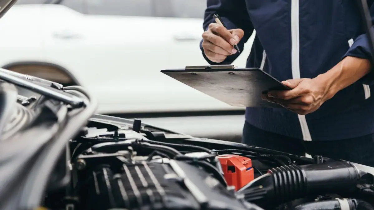 Mecânico inspecionando motor de carro com prancheta